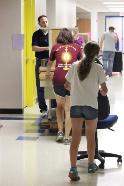 Business teacher David Dennis, along with two of his children, moves desks and chairs from the weight room to his new classroom on Aug. 10. (Photo by Webber)