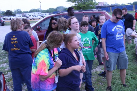 Students and staff members observe kite-flying from the edge of the field. 