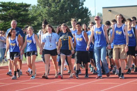 The front row of the cross country team holding hands as they make their way down the track.