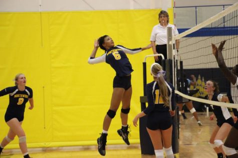 Junior Dajanae Arnold jumping up to spike the ball while Junior Lucy Herter behind her waiting for the bounce-back and Senior Katie Darnell previously setting the ball to Arnold.