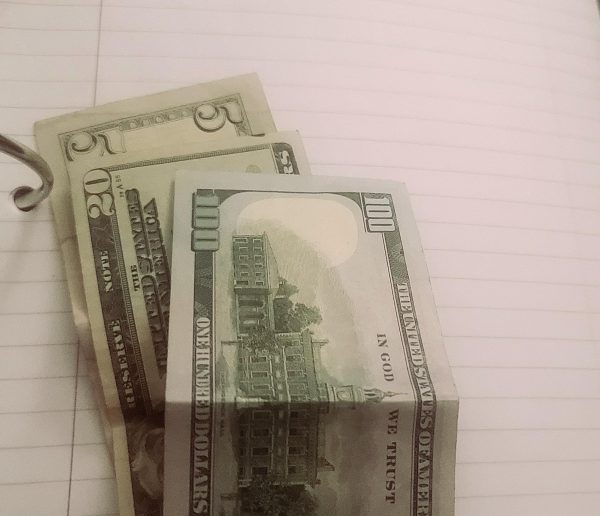 Picture of a 5, 20, and 100-dollar bill on top of a sheet of lined notebook paper in a binder.